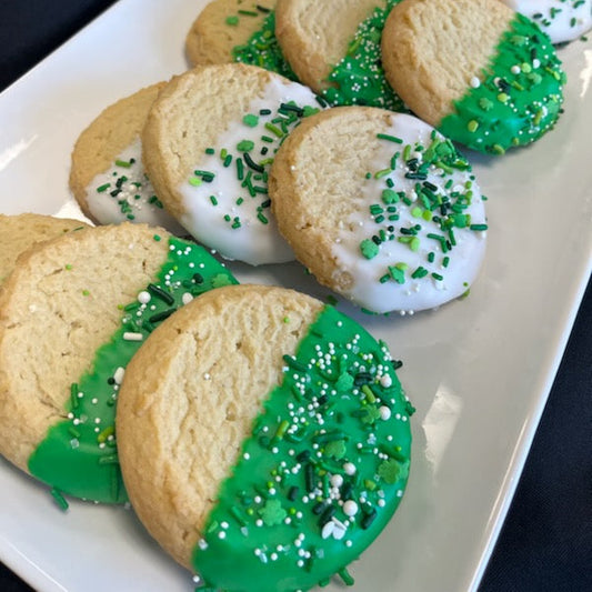 Dipped sugar cookies half-coated in green and white chocolate and topped with green and white sprinkles and jimmies, displayed on a white plate.