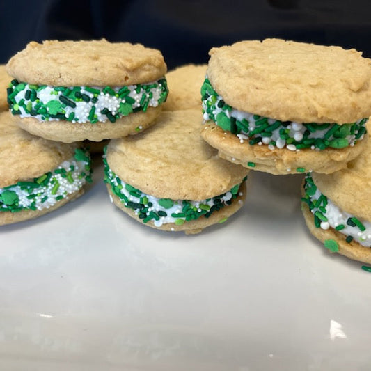 Sugar cookie whoopie pies with fluffy frosting filling rolled in green and white sprinkles, arranged on a white plate.