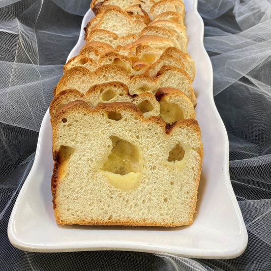A close-up of sliced cheddar cheese bread on a white rectangular plate, showing a golden crust and pockets of melted cheese throughout the interior.
