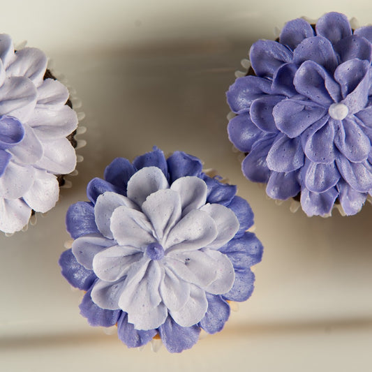 A top view of cupcakes topped with purple frosting piped in a layered floral petal design.