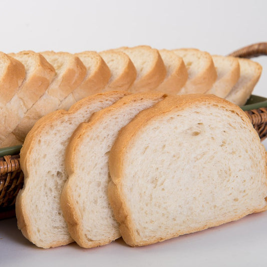 A close-up of sliced sourdough bread with the full loaf in a wicker basket tray visible in the background.