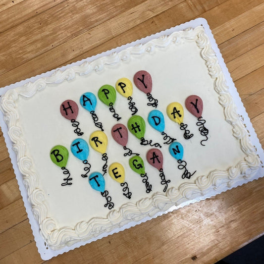 A half sheet decorated cookie with white frosting and scalloped border, decorated with colorful balloon clusters where each balloon contains a letter spelling out "Happy Birthday Tegan."