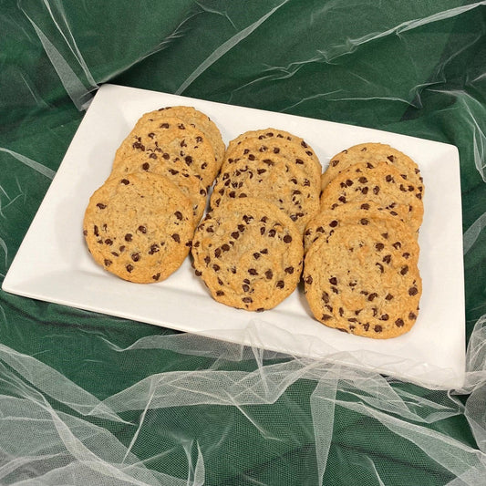 A close-up of vegan chocolate chip cookies on a white plate against a green background.