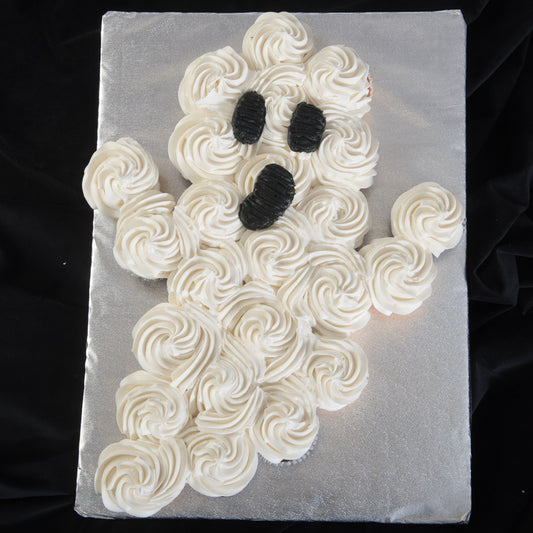 Pull-apart cupcake cake shaped like a friendly ghost with white swirled frosting and black oval eyes and mouth on a silver board.
