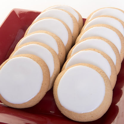 Twelve sugar cookies, topped with smooth white icing, arranged together in two rows on a red plate.
